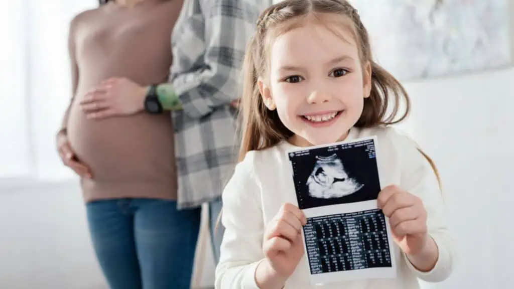 little girl holding an ultrasound with pregnant mom and dad