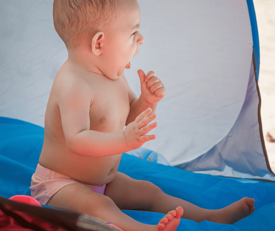 happy baby sitting protected in her beach tent