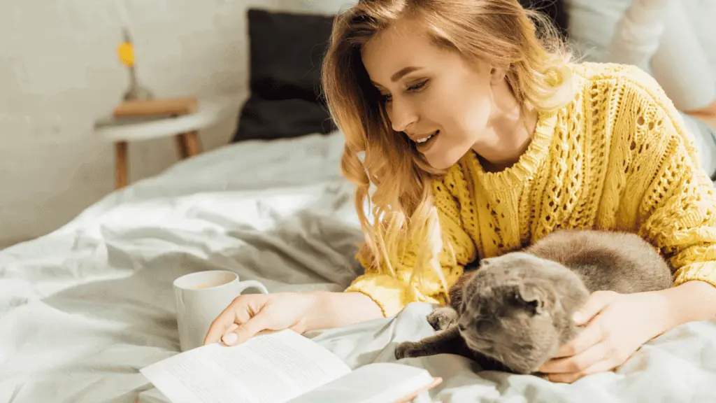 woman on bed reading with her cat coffee happy