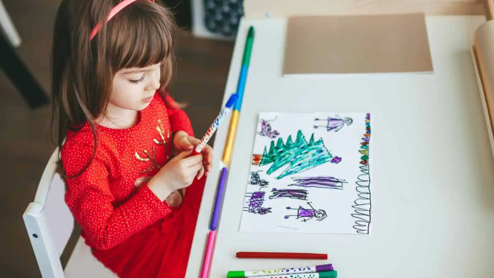 A little girl's imagination in a vibrant red dress joyfully sketching a Christmas-themed
