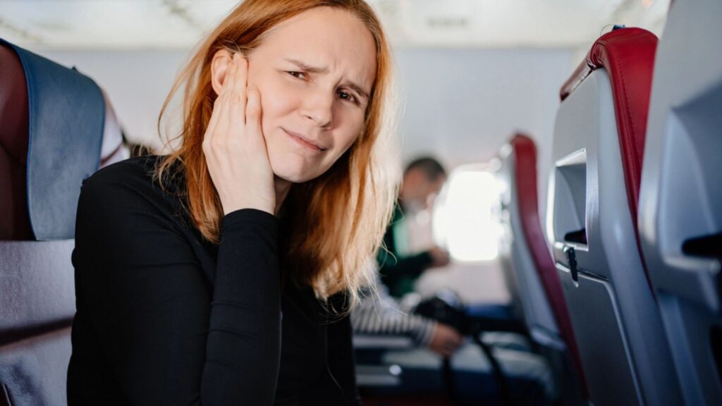A woman on an airplane has a headache and an earache while flying on airplane