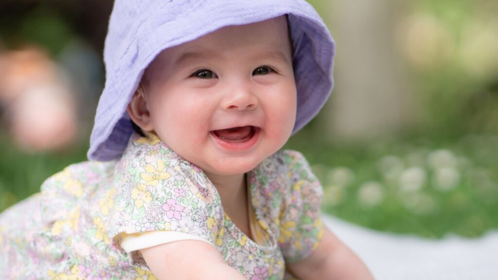 Adorable and happy baby girl in summer hat embraces the joys of playfulness on a soft blanket