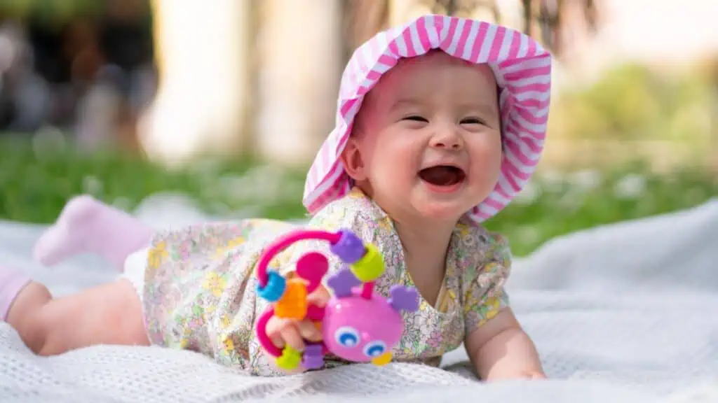Adorable and happy baby girl in summer hat embraces the joys of playfulness on a soft blanket playing with little toy