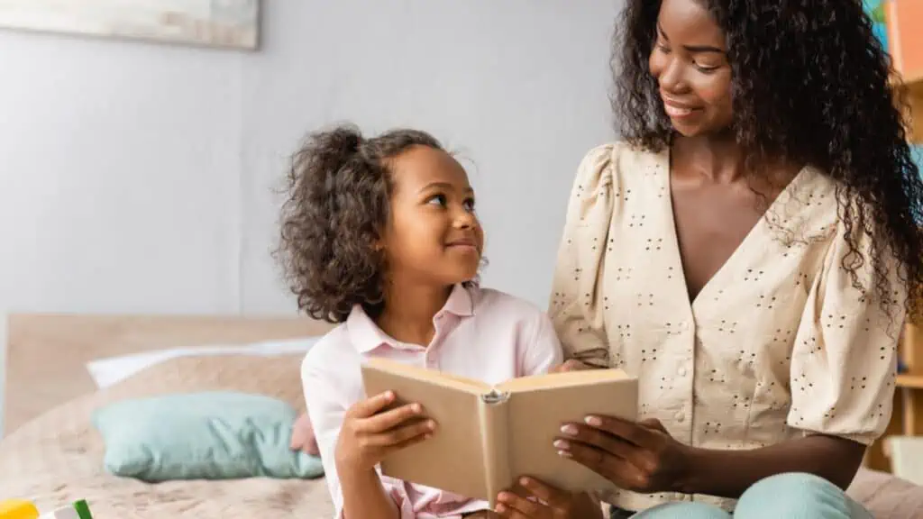 African american mom and child looking at each other while reading book