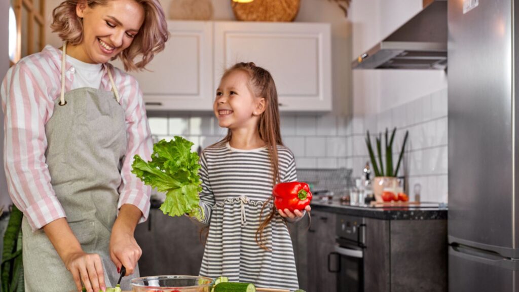 Attractive young single mother making a salad in the kitchen with her daughter