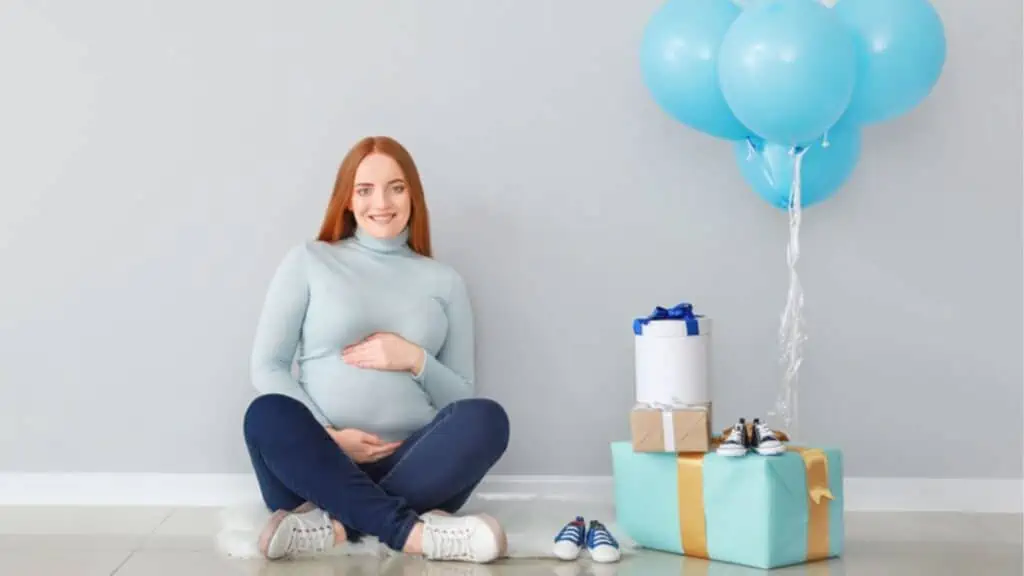Beautiful pregnant woman with baby shower gifts near light wall