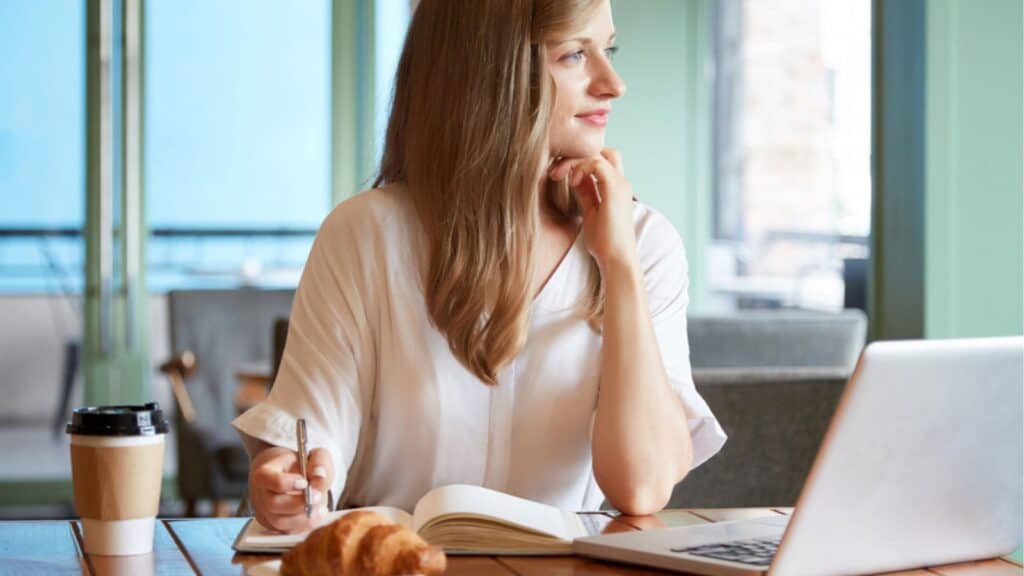 Beautiful woman thinking laptop on cafe table with coffee and croissant