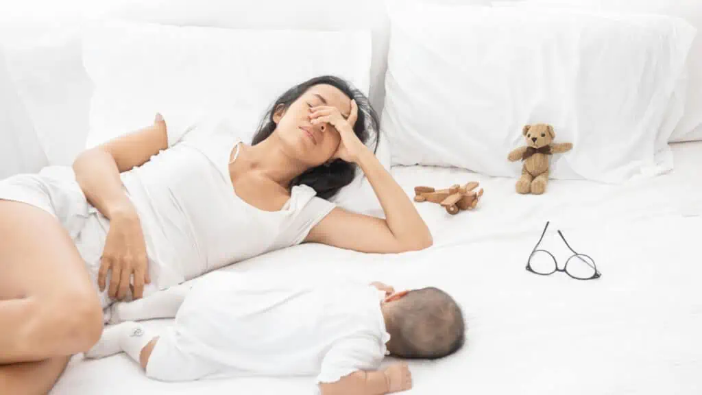 tired mom on white bed with baby