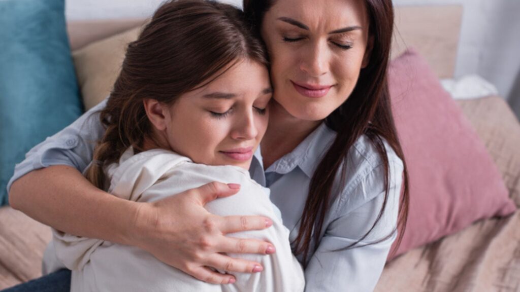 Caring mother embracing teenage daughter in bedroom
