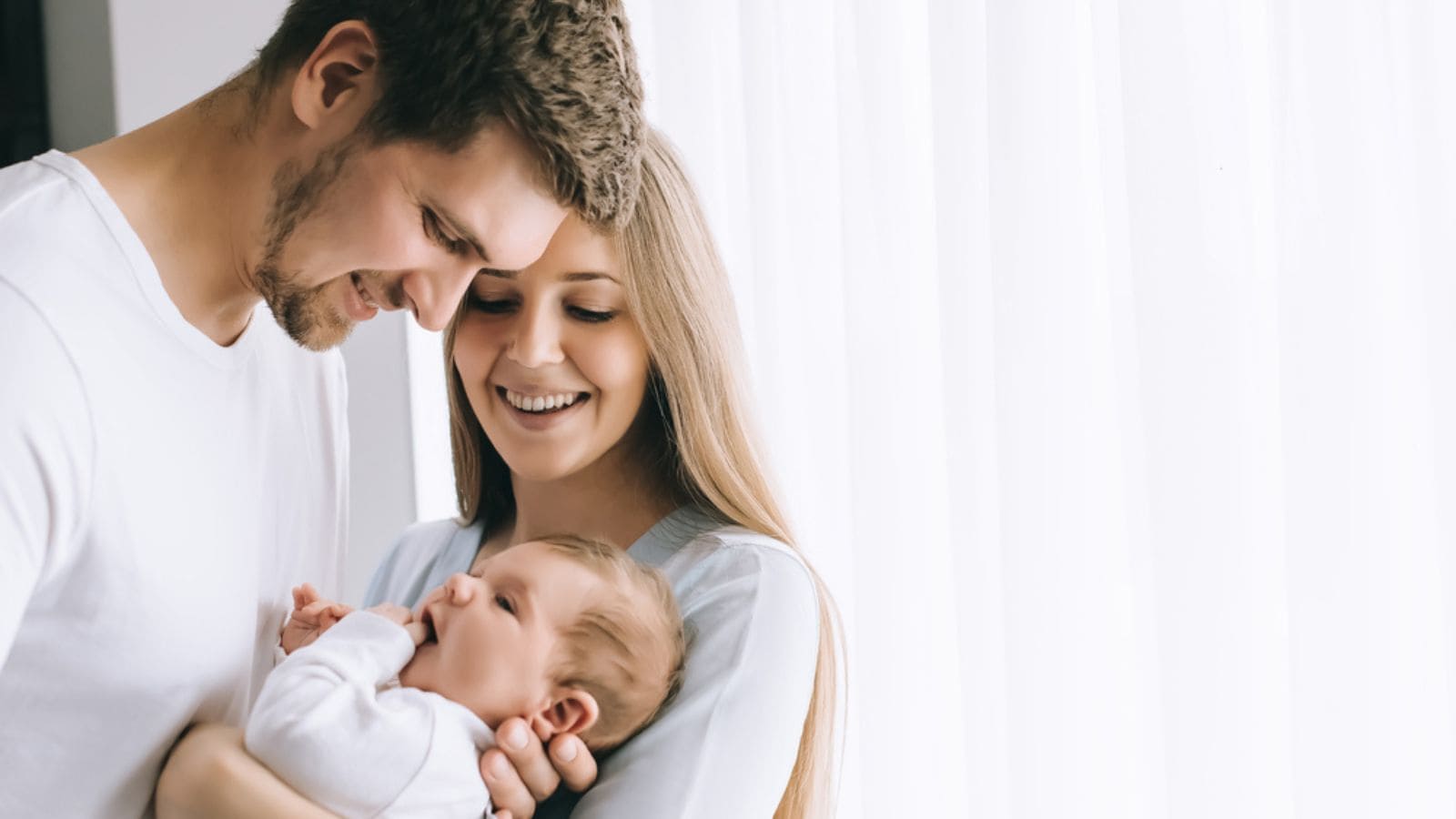Cheerful family carrying little baby boy in front of curtains at home