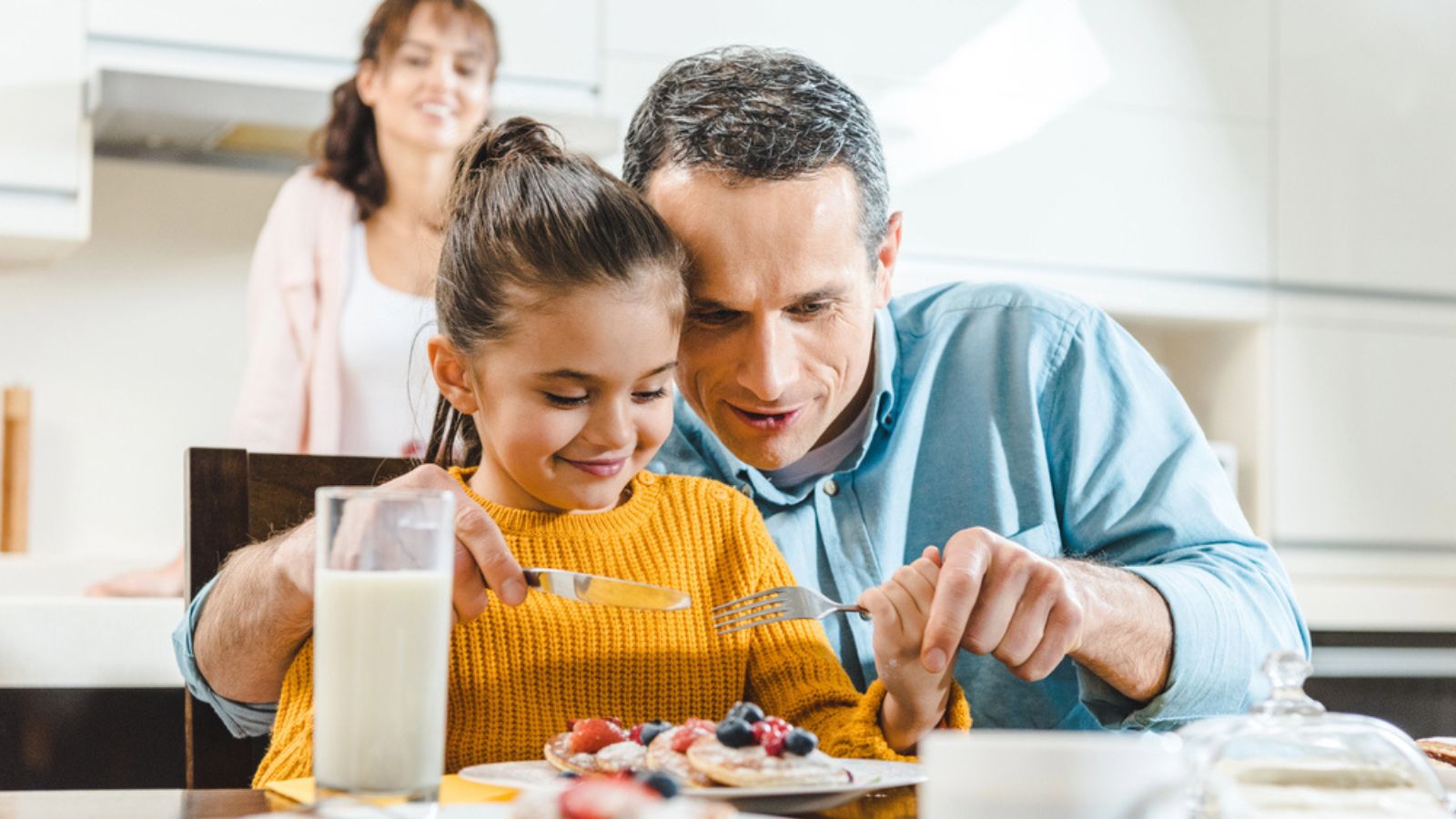 Cheerful family together eating pancakes with berries at table on kitchen