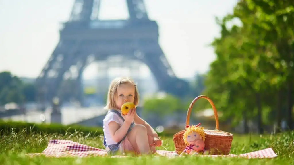 Cheerful toddler girl having picnic near the Eiffel tower in Paris