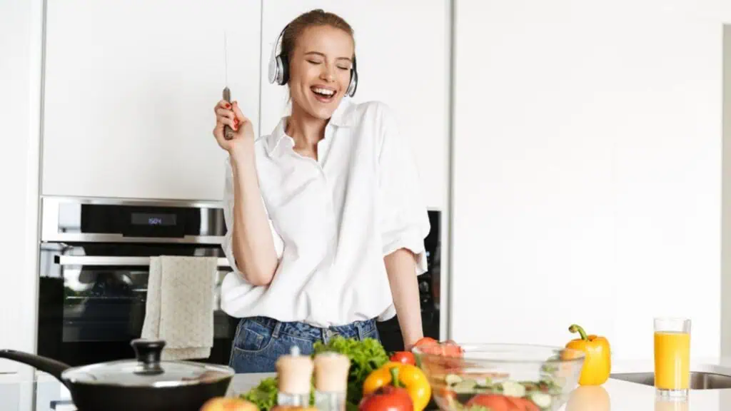 Cheerful young woman listening to music with headphones while cooking
