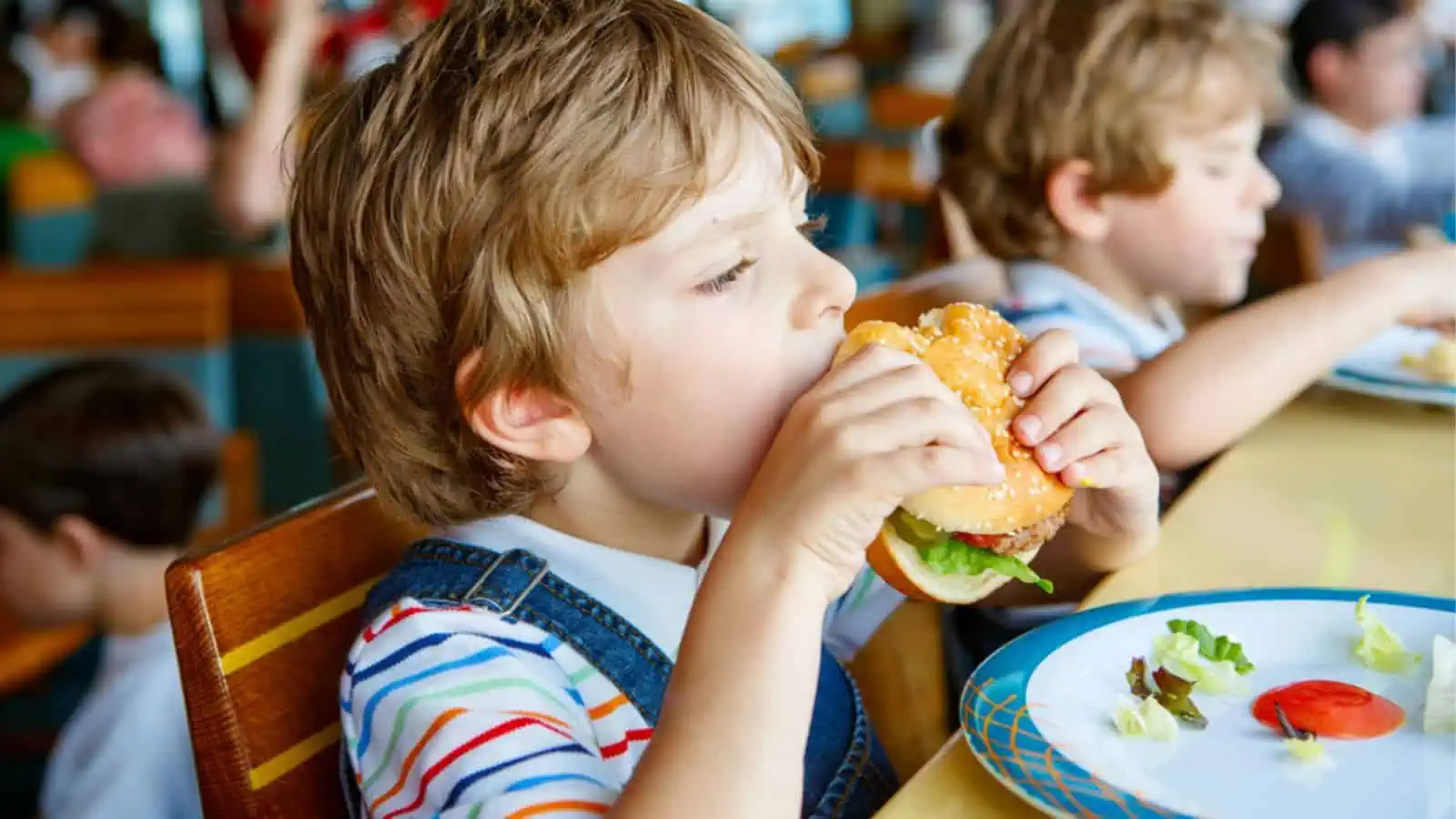 Child eating burger sitting in school canteen