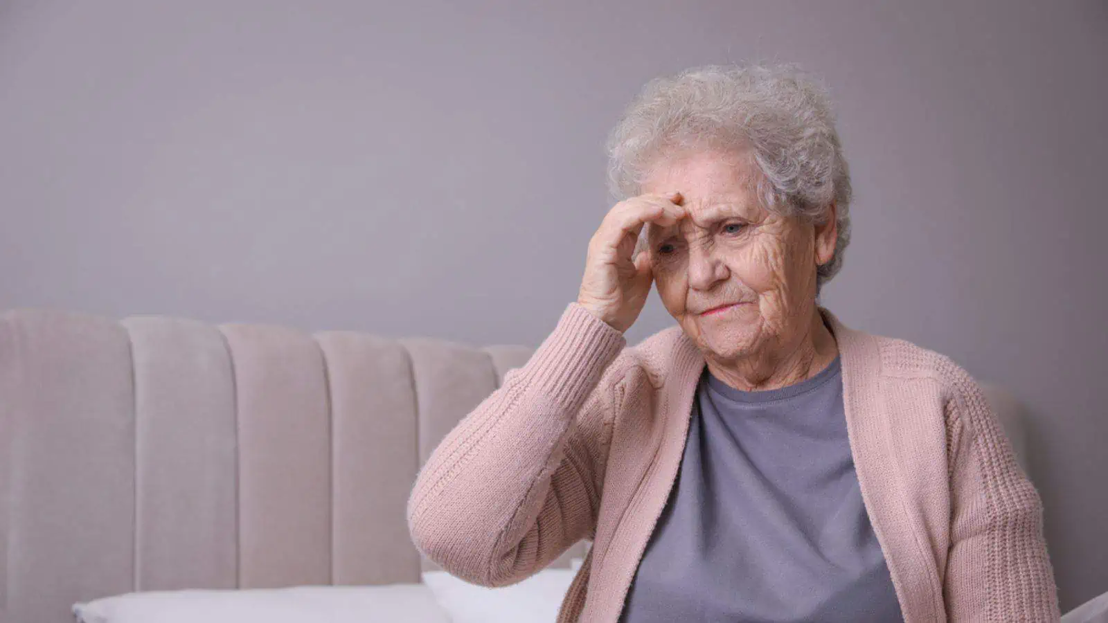 Confused old woman with headache in bedroom at home