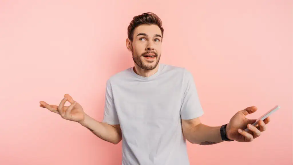 Confused young man showing shrug gesture in pink