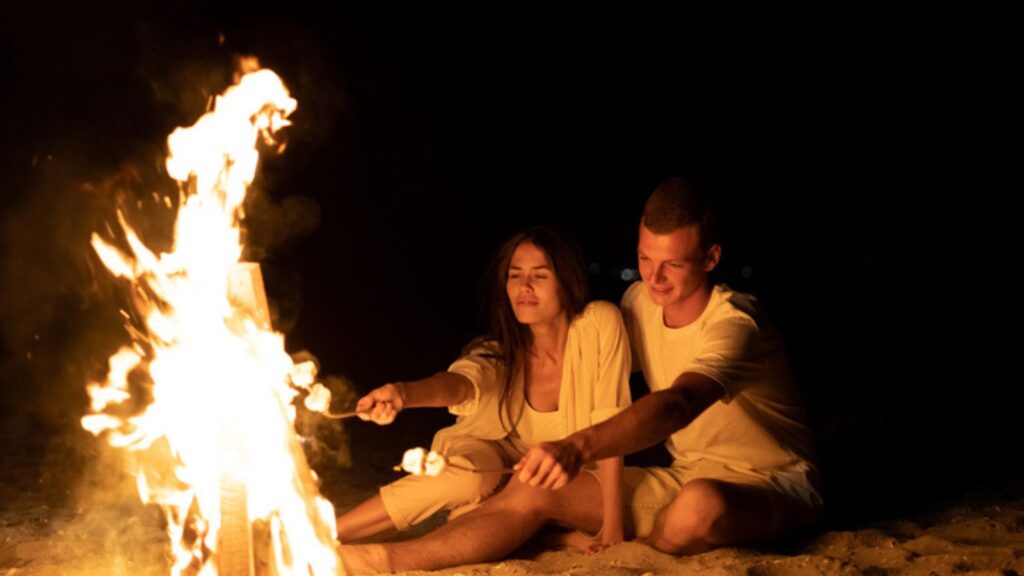 Couple date on the seashore sits by the fire and toasts marshmallow on a stick