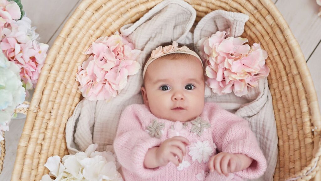 Cute baby girl in knitted clothes and wreath with teddy bear toy