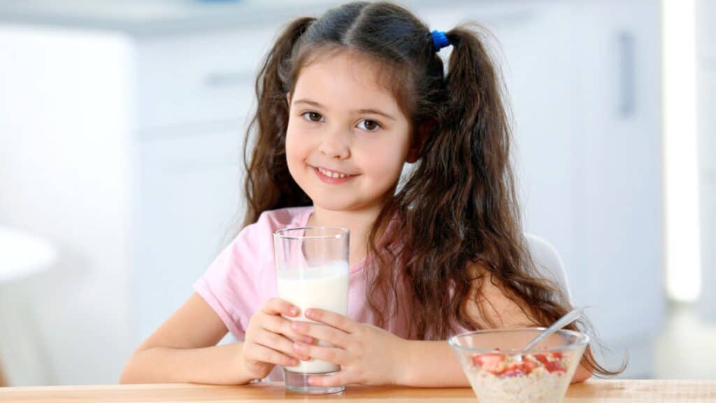 Cute little girl with milk and healthy breakfast at table in kitchen