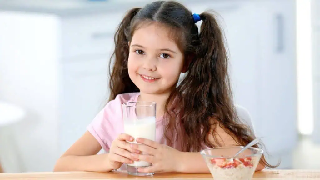 Cute little girl with milk and healthy breakfast at table in kitchen