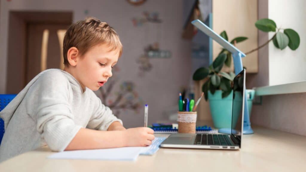 Cute little schoolboy studying at home doing school homework while using laptop