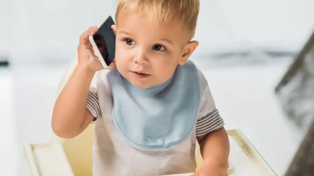 Cute toddler talking on smartphone and sitting in baby chair