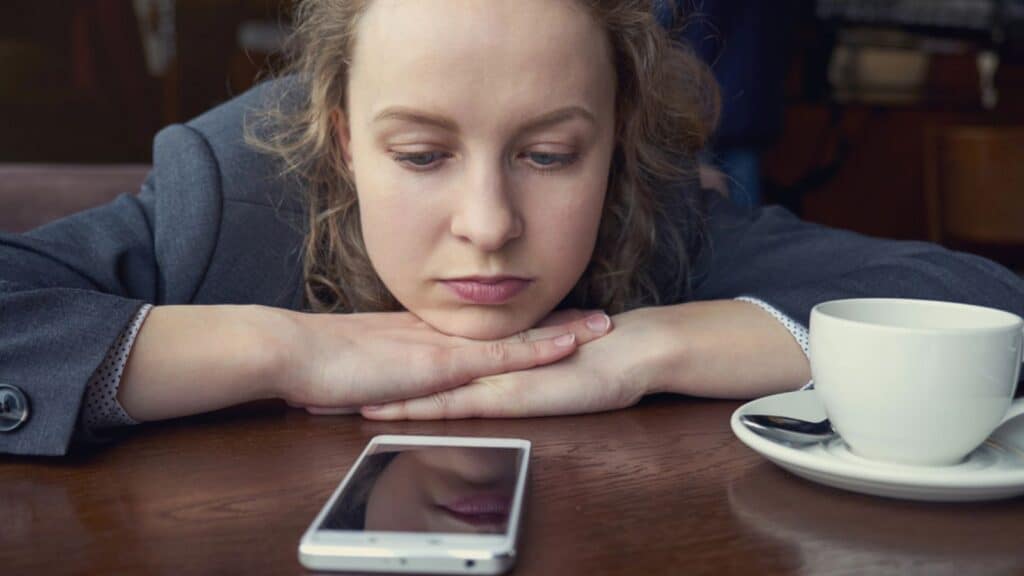 Disappointed sad woman looking at phone and waiting message or call