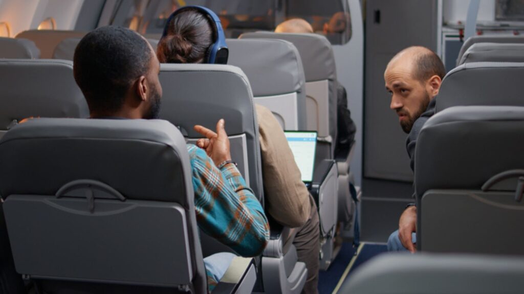 Diverse travellers man having conversation in airplane before takeoff,