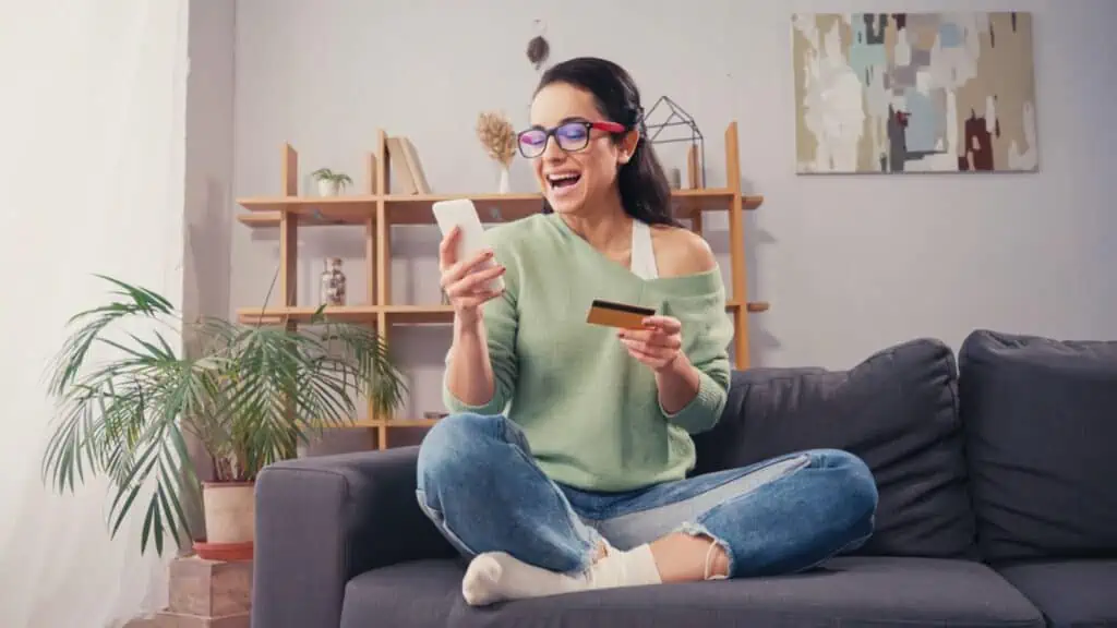 Excited Woman Eyeglasses Using Smartphone Credit Card