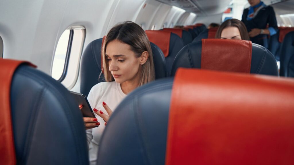 Female in plane cabin clicking on her smartphone