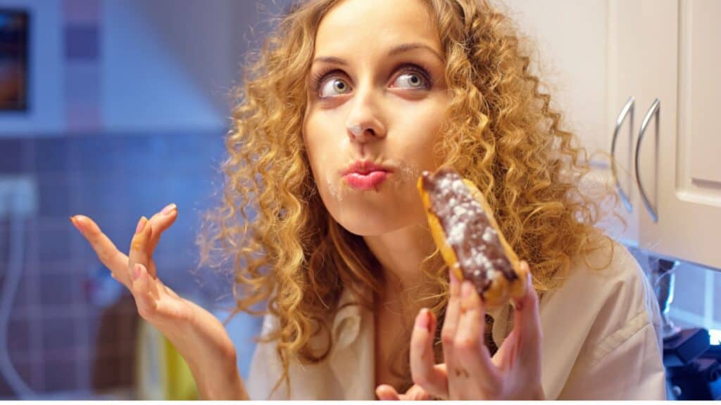 Funny young woman eating sweet cake in the kitchen at night