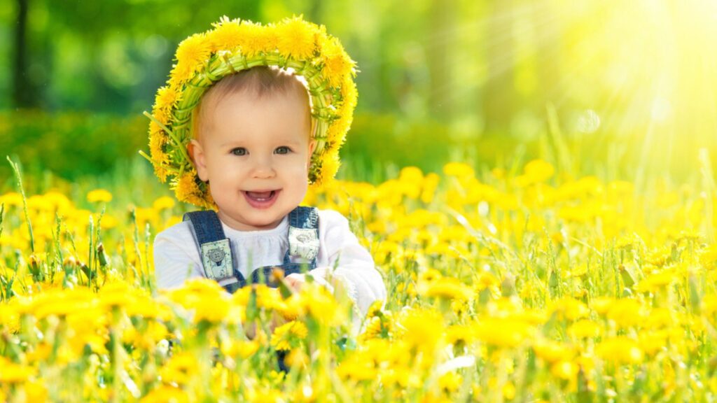 Happy baby girl in a wreath on meadow with yellow flowers with a sun light