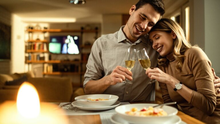 Happy couple embracing and toasting with Champagne while having dinner at dinning table