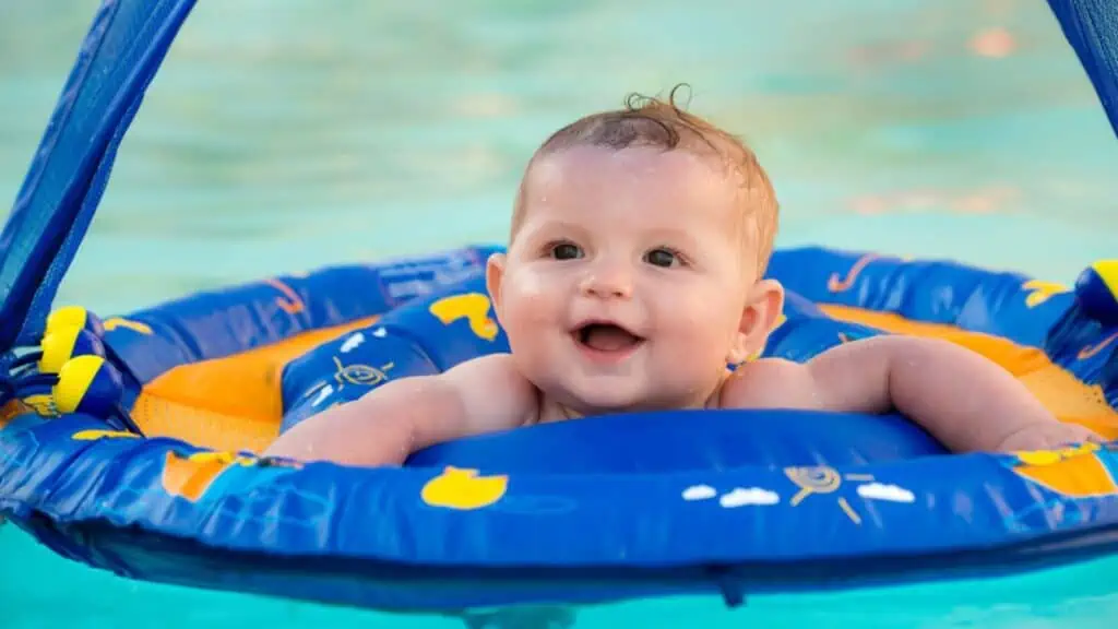 Happy infant playing in pool while sitting in baby float with canopy