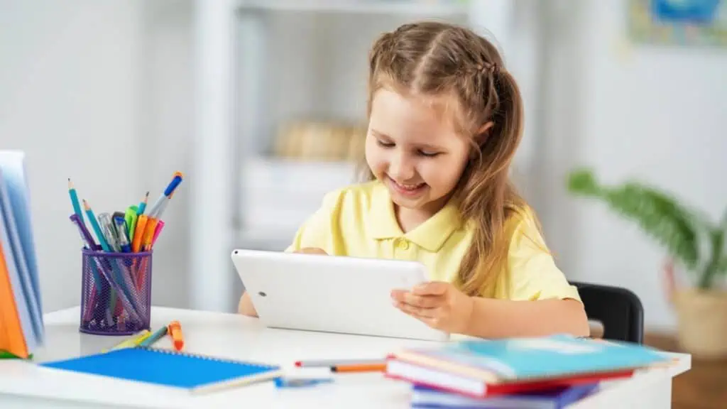 Happy little schoolgirl sitting at her Desk using her tablet