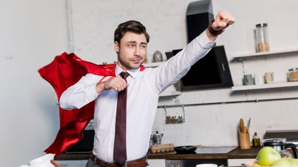 Happy man in superhero red cloak posing in kitchen at home