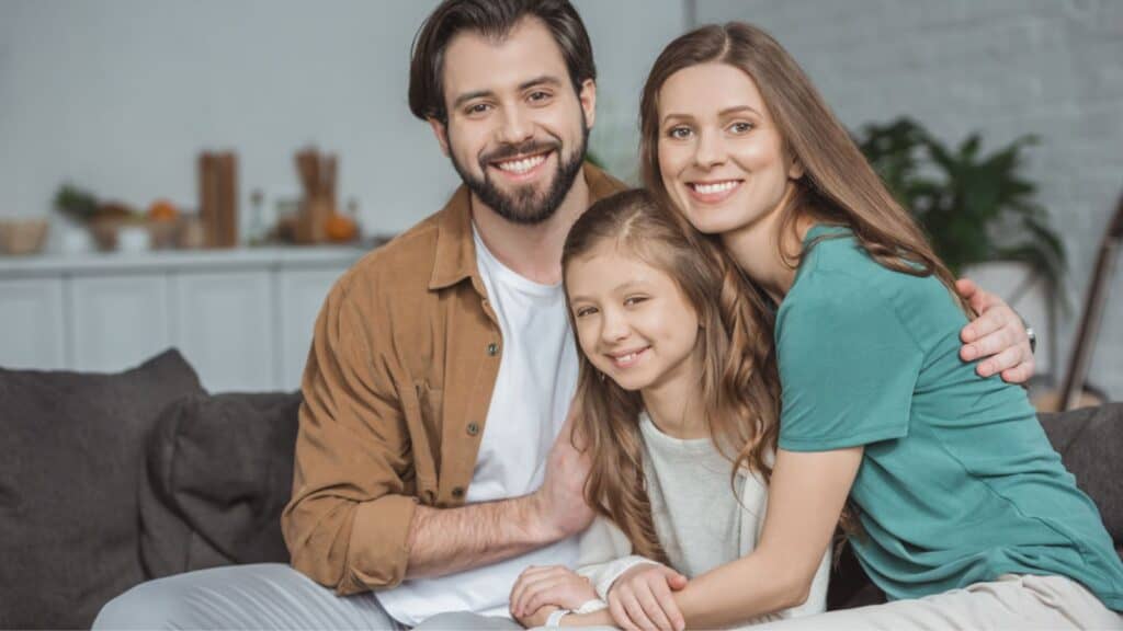 Happy parents and daughter looking at camera at home
