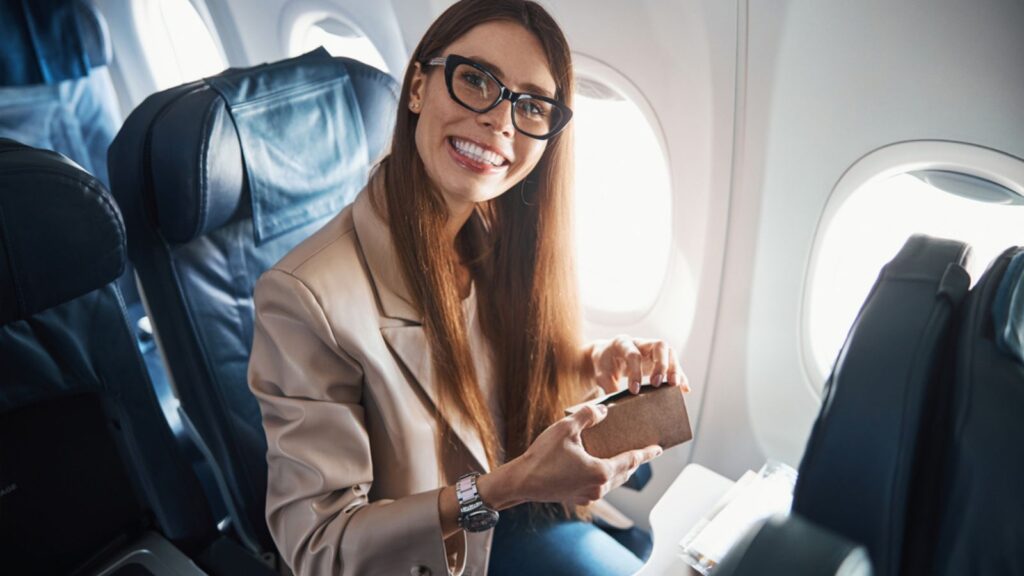 Happy woman sitting near plane window while holding her wallet
