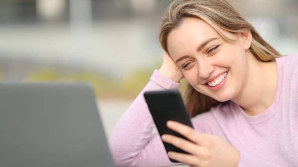 Happy woman using smart phone and laptop sitting in the street