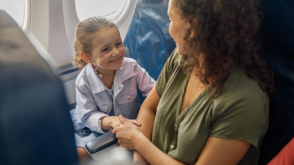 High angle view of little girl sitting on the plane, smiling to her mother while they are traveling together. Family, vacation concept