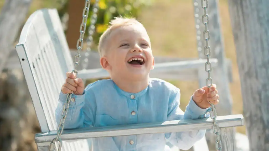 Laughing boy swinging on a summer sunny day