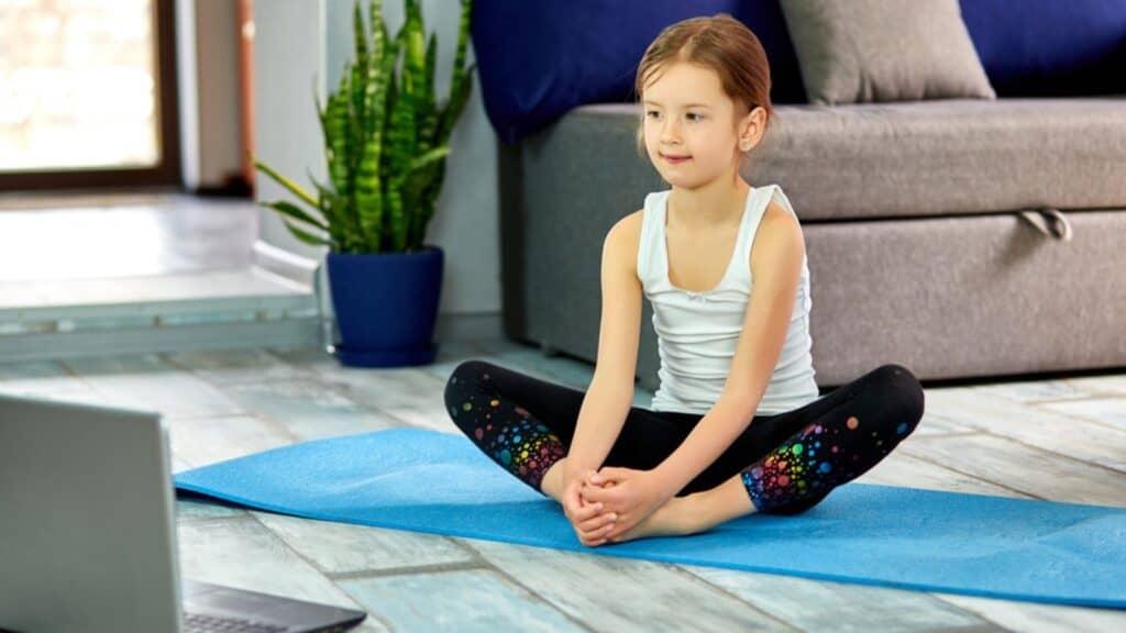 Little cute girl in sportswear on blue mat practicing gymnastics at home