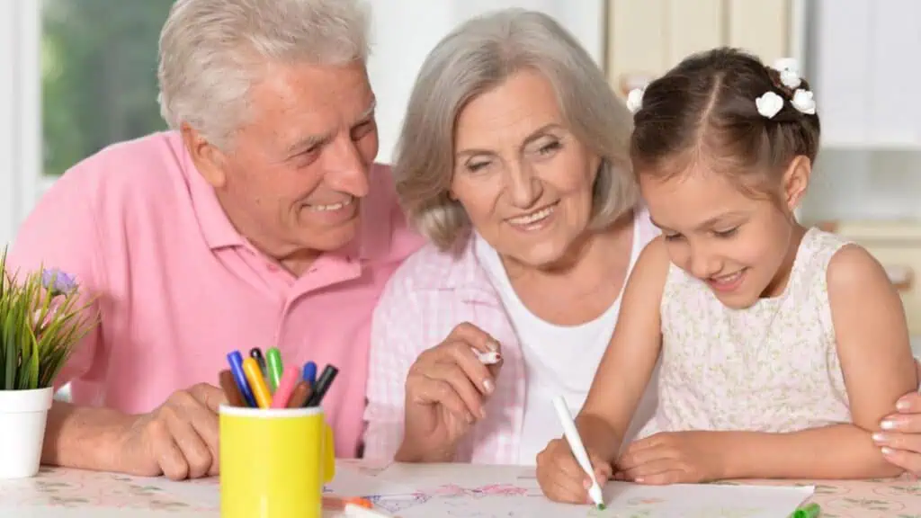 Little cute girl with grandparents drawing at the table at home