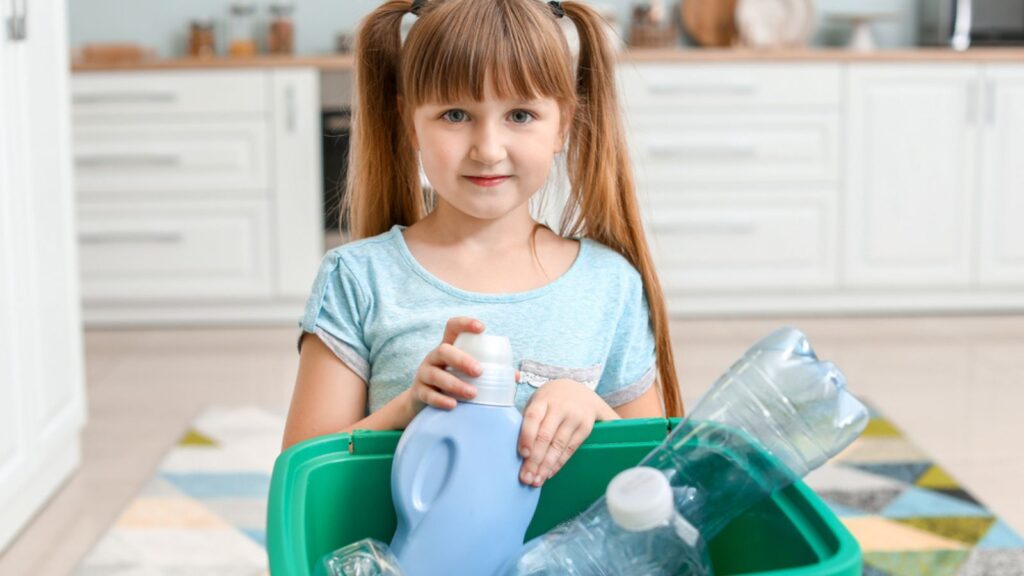 Little girl and container with trash in kitchen