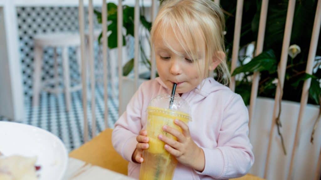 Little girl drinking orange juice in a cafe