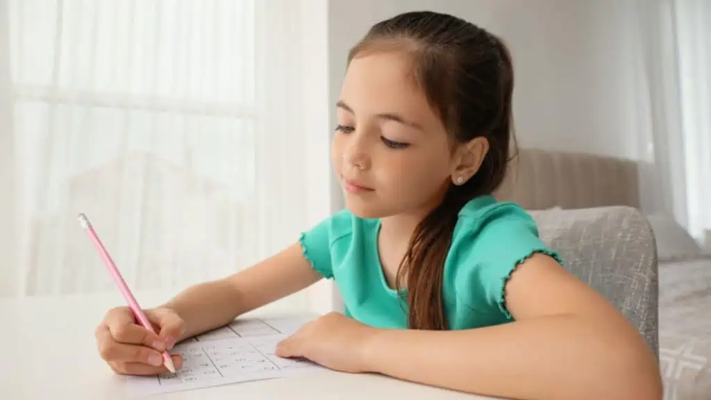 Little girl solving sudoku puzzle at table indoors