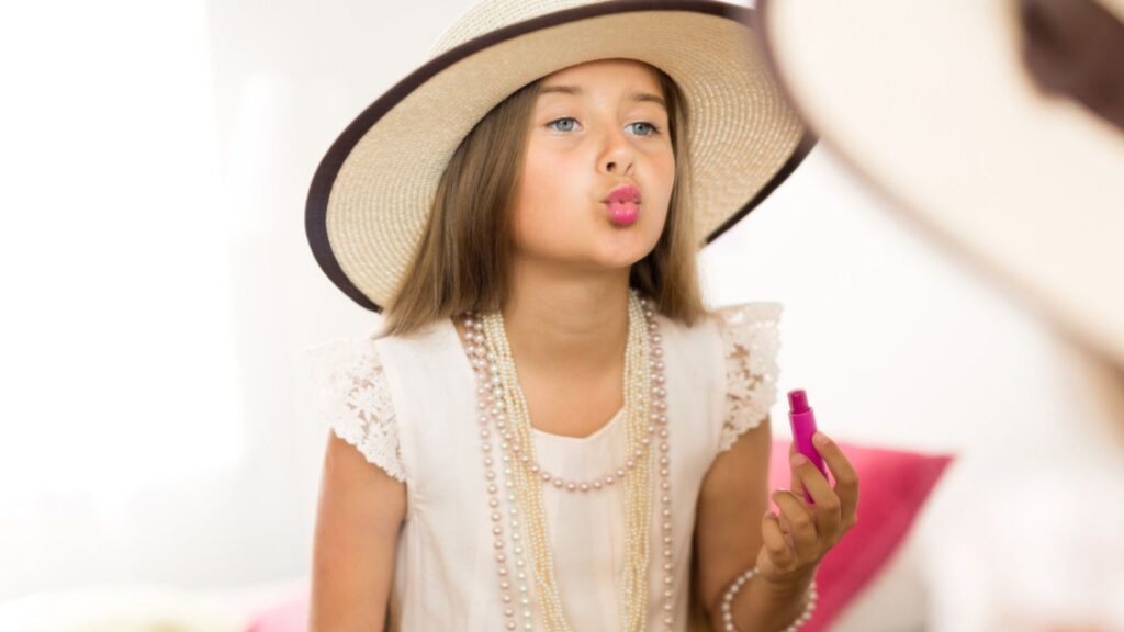 Little girl with lipstick looking at mirror
