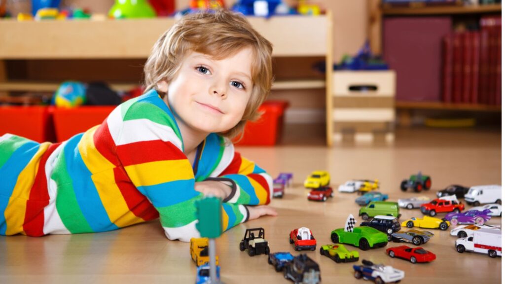 Lovely blond kid boy playing with lots of toy cars indoor