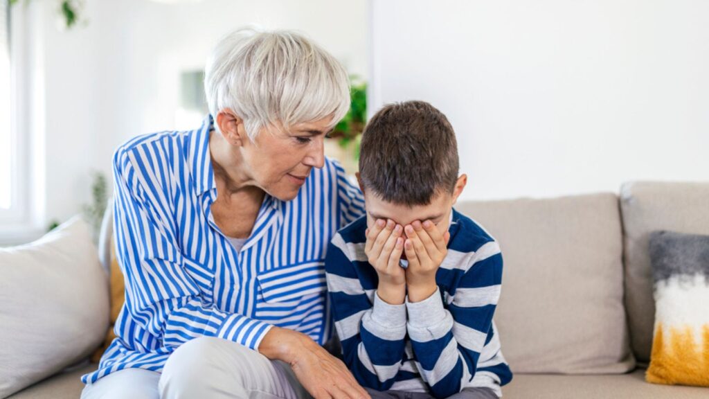 Loving understanding old grandma embracing little crying boy comforting upset grandson