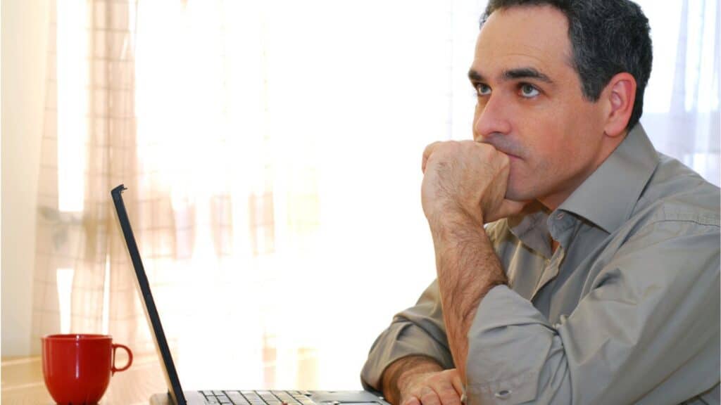 Man sitting thinking at a desk and looking into his computer
